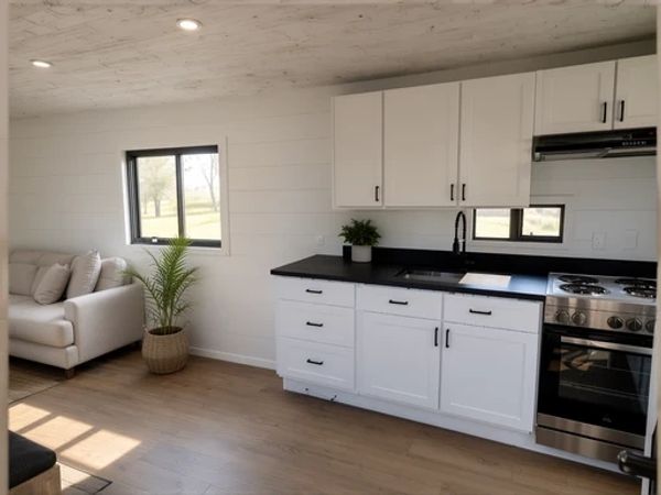 Modern minimalist kitchen and living area with white cabinets and black countertop.