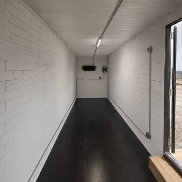 Empty narrow room with white walls and black floor.
