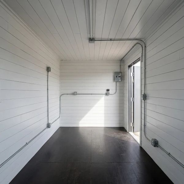 Empty room with white paneled walls and dark floor.