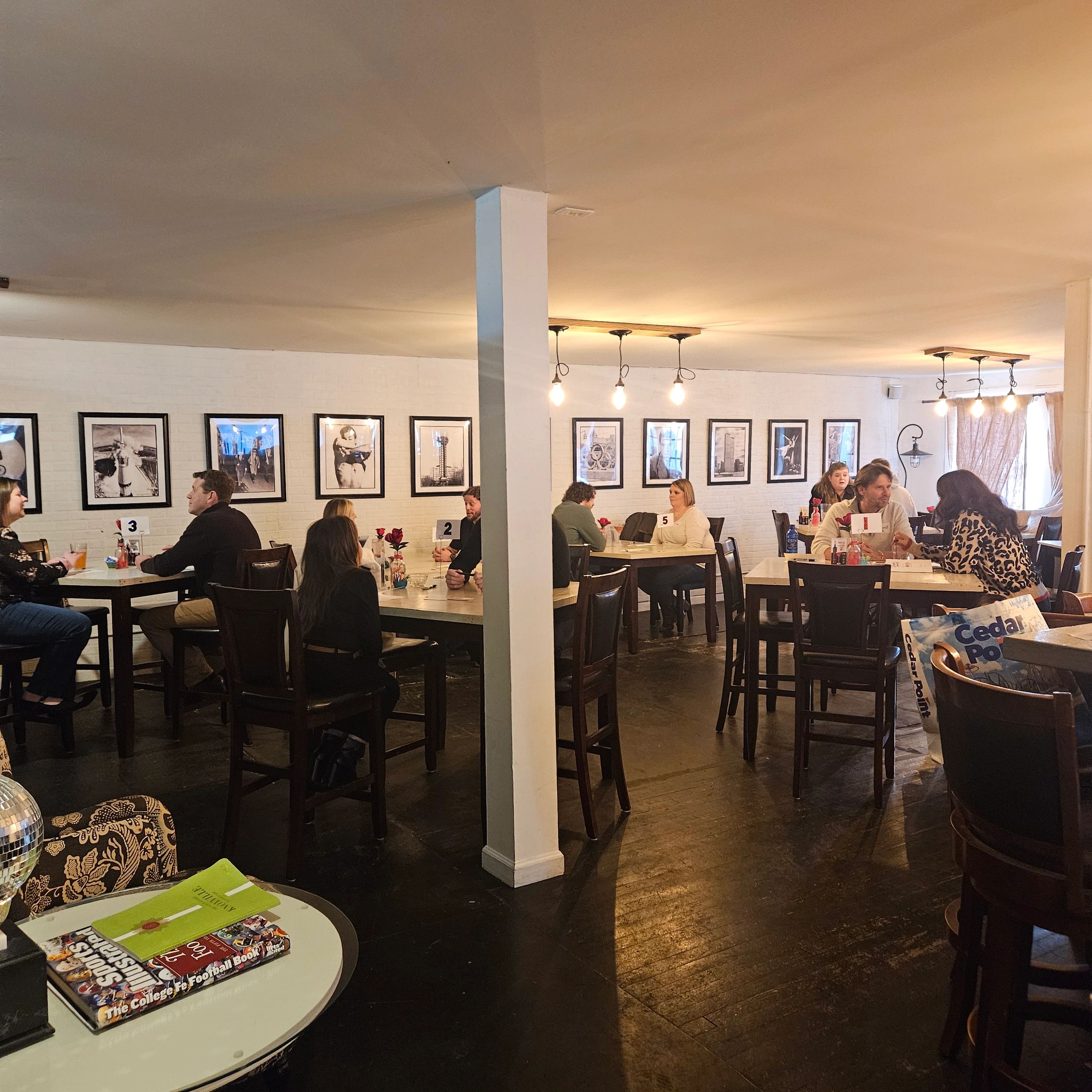 People dining and socializing in a cozy room with framed pictures on white walls.