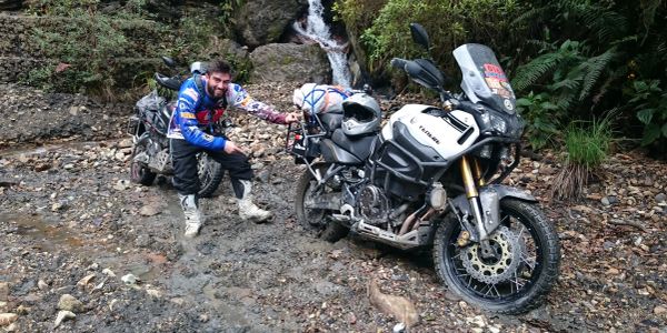 Motociclista junto a dos motos en camino rocoso.