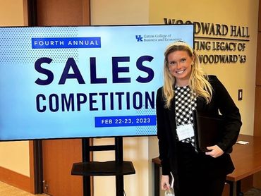 A woman stands next to a sign for the Fourth Annual Sales Competition.