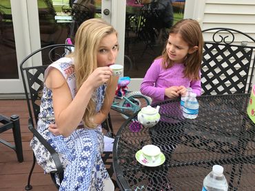 A woman and a girl enjoy tea at an outdoor table.