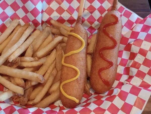 Two corn dogs with mustard and ketchup, served with fries.