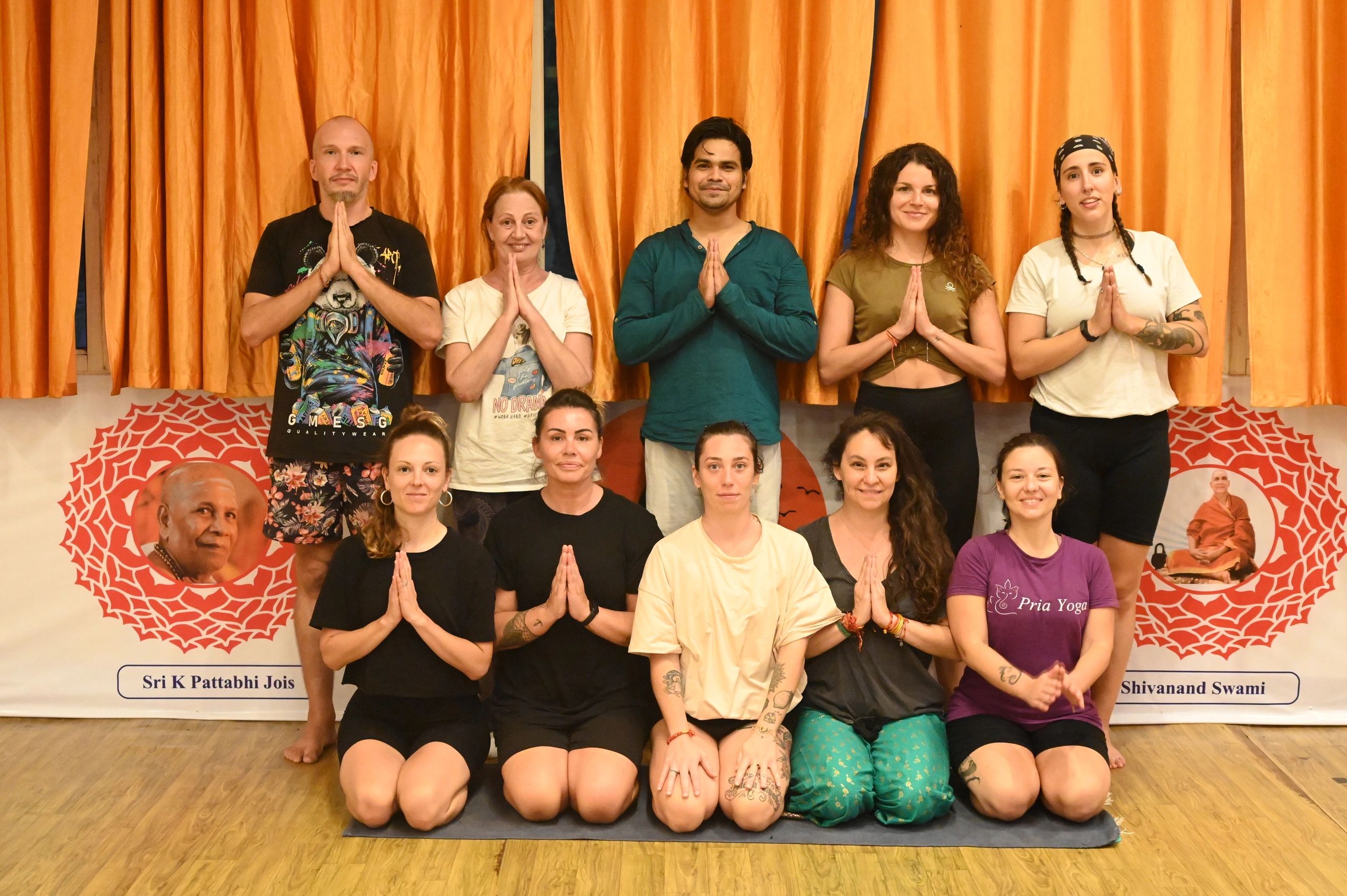Group of people posing in a yoga studio with hands in prayer position.