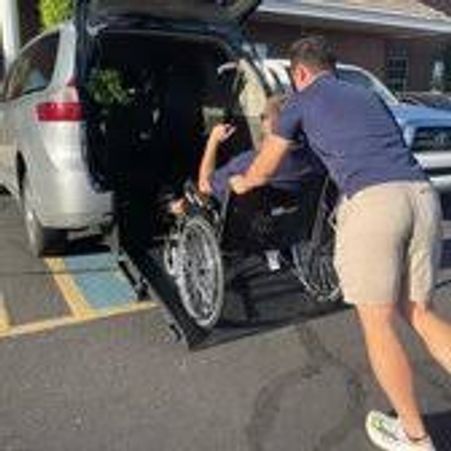 Man pushing person in wheelchair up a ramp into a van.