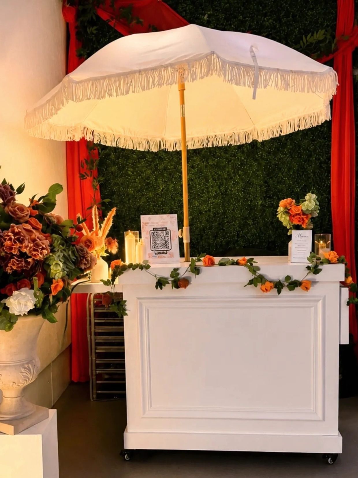White bar cart decorated with flowers and umbrella.