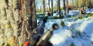 Person aiming with a rifle in a snowy forest.