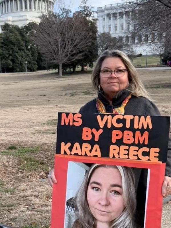 Woman holding a sign protesting PBM with a photo of Kara Reece.