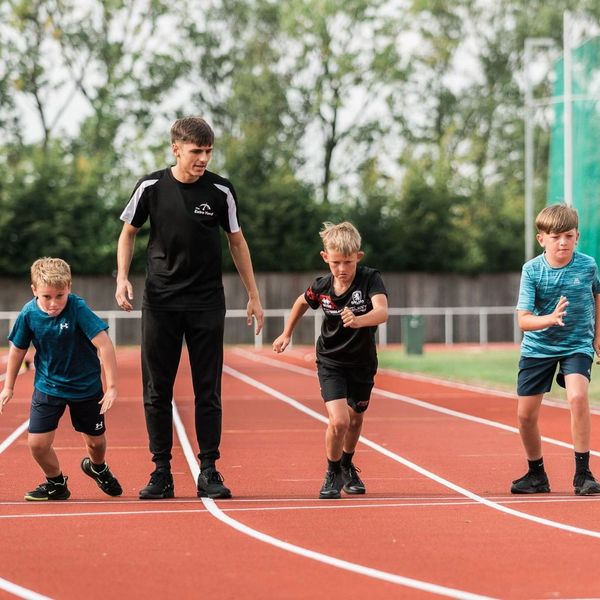 Young boys preparing to start a race on a track with a coach in the middle.