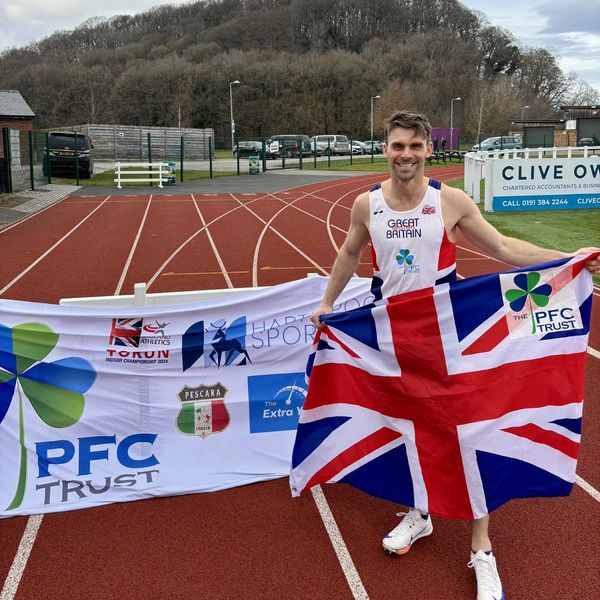 Athlete proudly holding British flag on running track with sponsor banners.