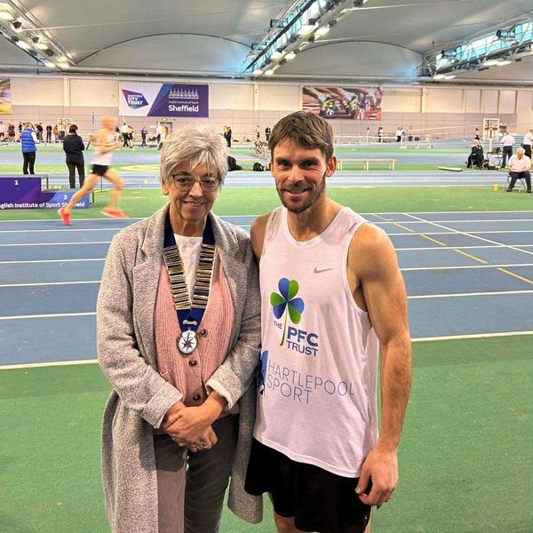 Athlete and official posing at an indoor sports facility with a running track.