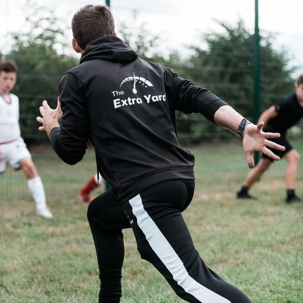 Man in black sportswear stretching on grass with kids in background.