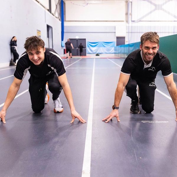 Two men smiling and getting ready to sprint on an indoor track.