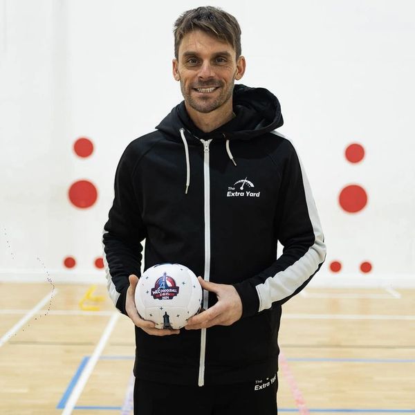 Man in black sportswear holding a dodgeball in a gymnasium.