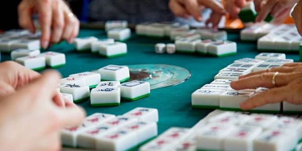 People playing Mahjong with tiles on a green table.