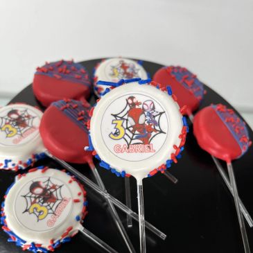 Spider-Man themed birthday cake pops with red, blue, and white icing and sprinkles.