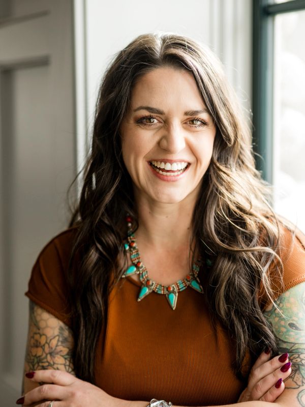 Smiling woman with long hair and tattoos wearing a turquoise necklace.