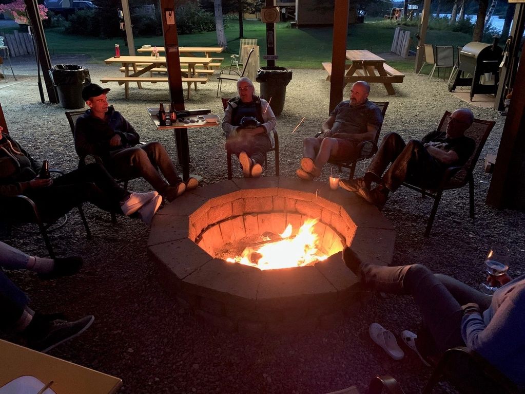 Group of people relaxing around a fire pit at night outdoors.