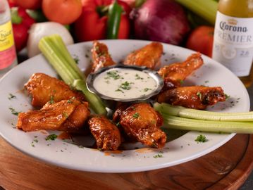 Buffalo chicken wings with celery and ranch dip on a white plate.
