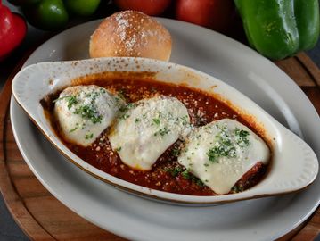 Baked dish with melted cheese and tomato sauce, served with a bread roll.