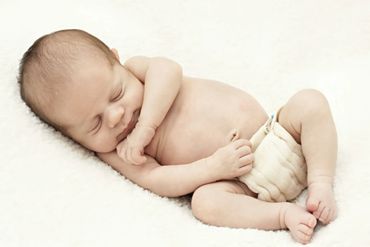 Peacefully sleeping newborn baby wearing a diaper on a soft surface.