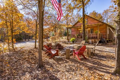 Cozy autumn cabin with a fire pit and red chairs under a waving American flag.