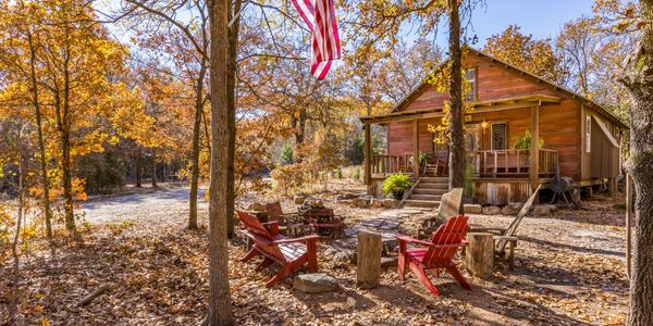 Cozy autumn cabin with a fire pit and red chairs under a waving American flag.