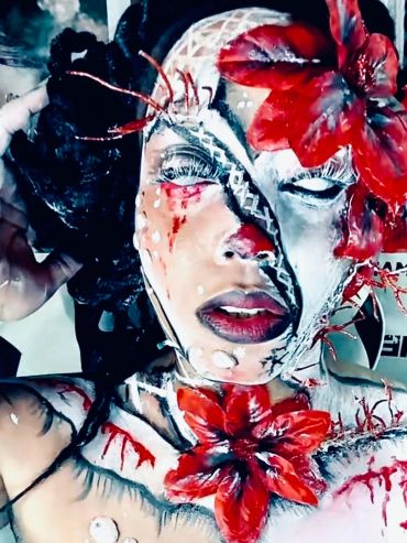 Person with intricate face and body paint featuring red flowers and white accents.
