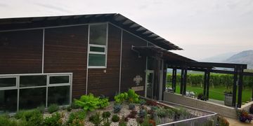 Modern winery building surrounded by lush gardens and vineyards under a cloudy sky.