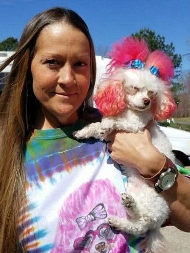 Woman holding a white poodle with pink and blue hair accessories.