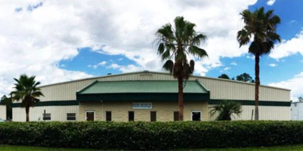 Industrial building with palm trees and cloudy sky background.