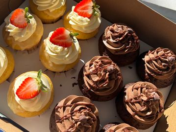 Box of vanilla and chocolate cupcakes with frosting and strawberries.