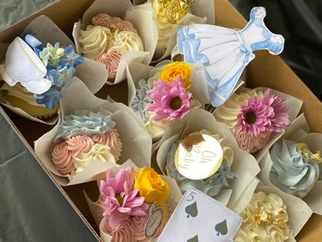 Decorated cupcakes with flowers, playing cards, and themed toppers in a box.