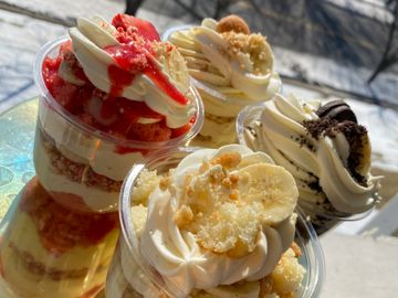 Four assorted layered dessert cups with cream and toppings on a reflective surface.