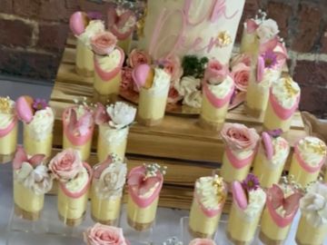 Elegant dessert display with creamy treats adorned with pink roses and macarons.