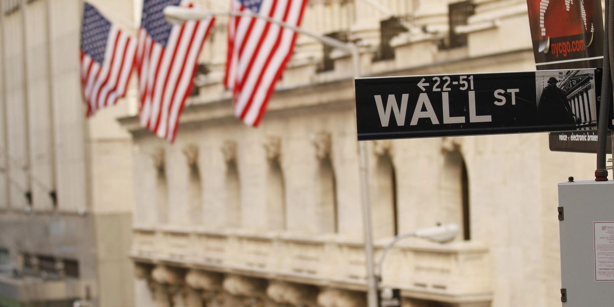 wall street sign with New York stock exchange blurred flags as background
