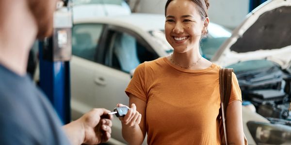 A woman happily receives car keys from a mechanic in a repair shop.