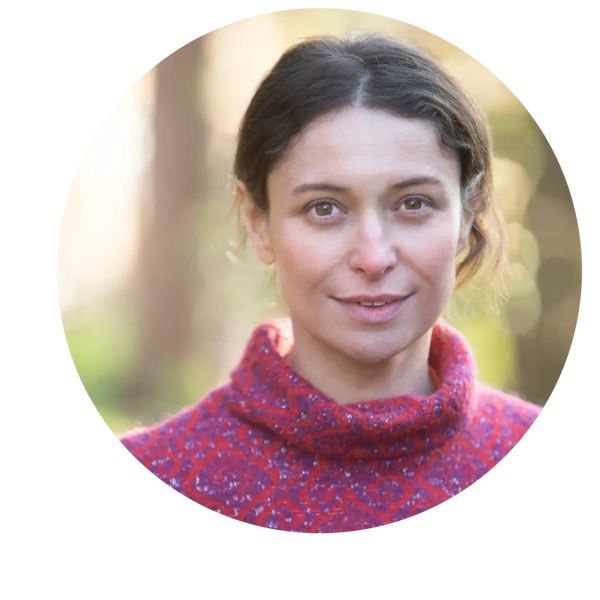 Smiling woman in a red patterned sweater outdoors with soft natural light.