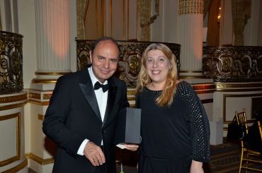 Man and woman posing with an award in a formal setting.