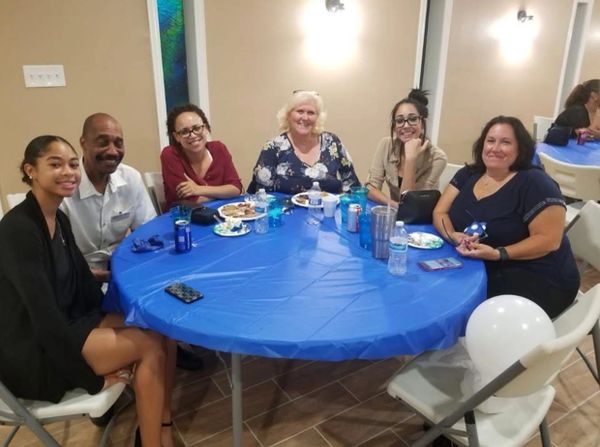 Six people smiling around a blue-covered table with food and drinks.