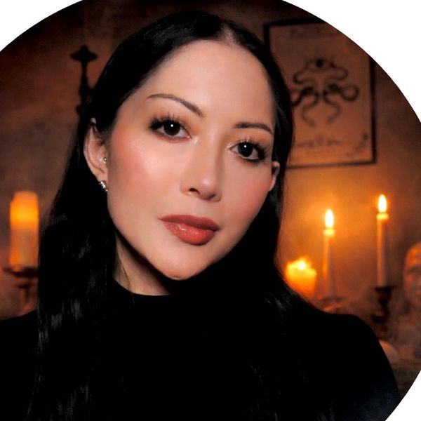 Woman with long dark hair poses in a dimly lit room with candles.