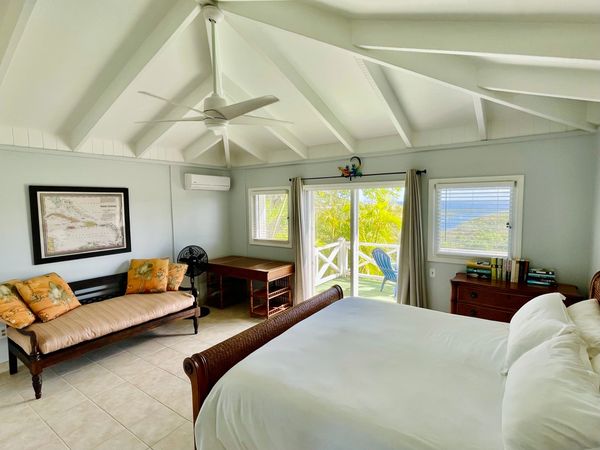 Bright bedroom with tropical decor and ocean view from balcony.