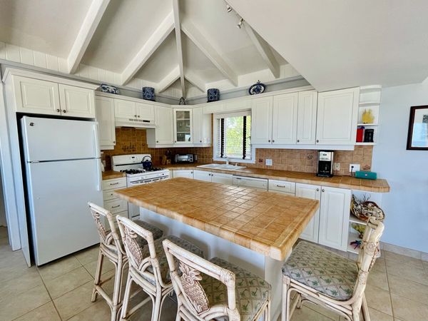 Bright kitchen with white cabinets, tiled countertops, and wicker bar stools.