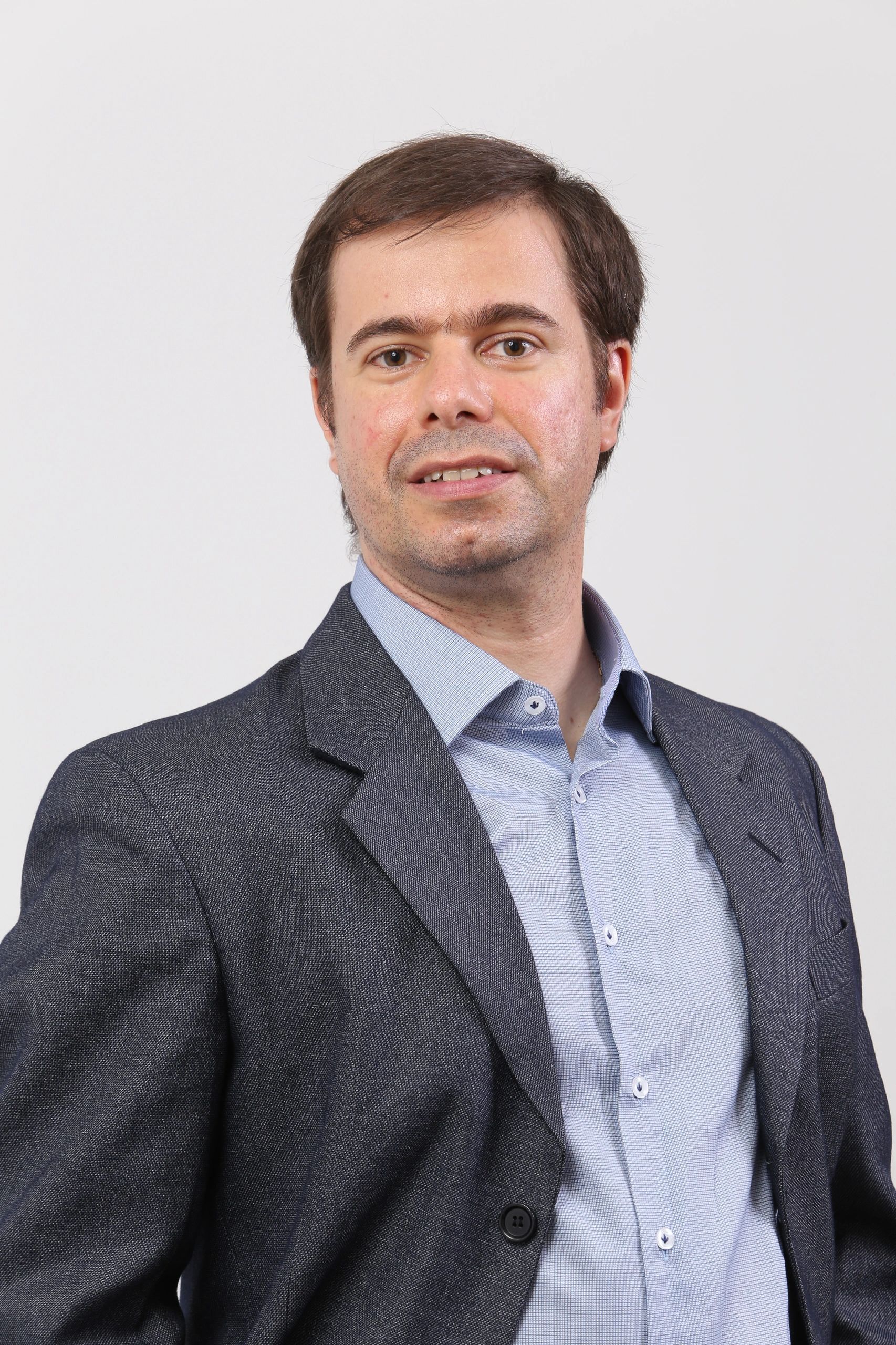 Man in a dark blazer and light blue shirt posing against a plain background.