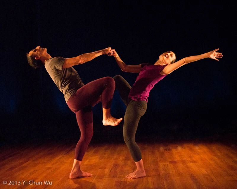 Two dancers connected and reaching in opposite directions