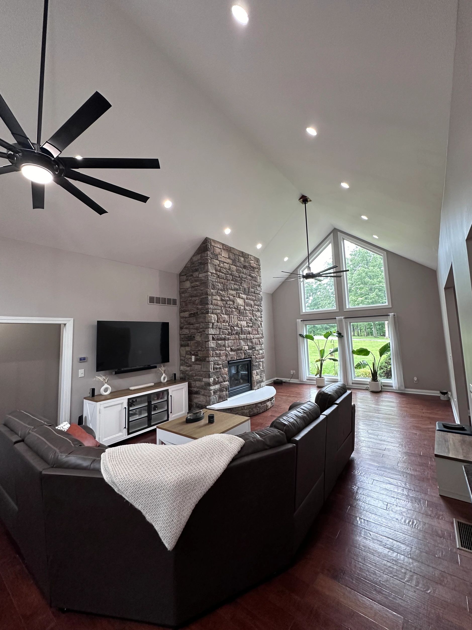 Modern living room with vaulted ceiling, stone fireplace, and large windows.