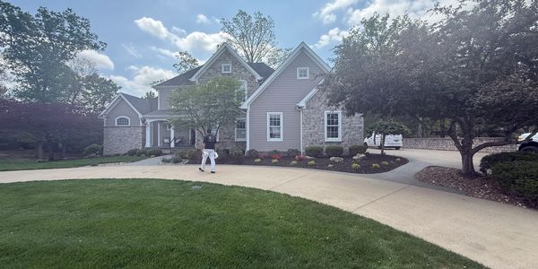 A large house with a person walking on the driveway under a blue sky.