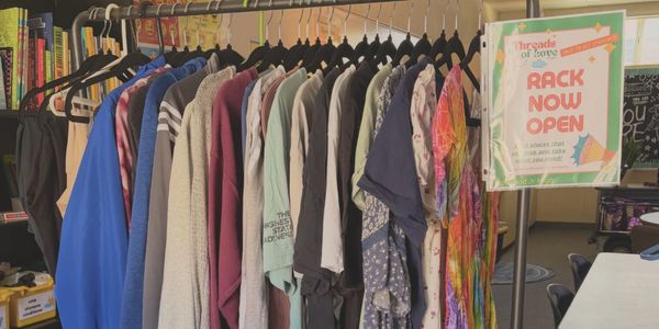 Clothes hanging on a rack with a sign.