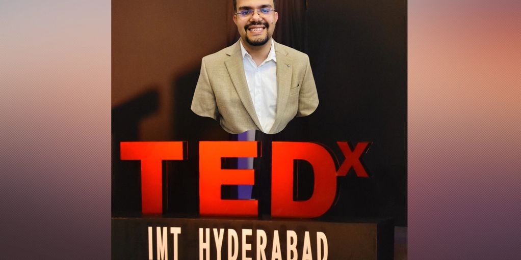 Man smiling behind a TEDx IMT Hyderabad sign.